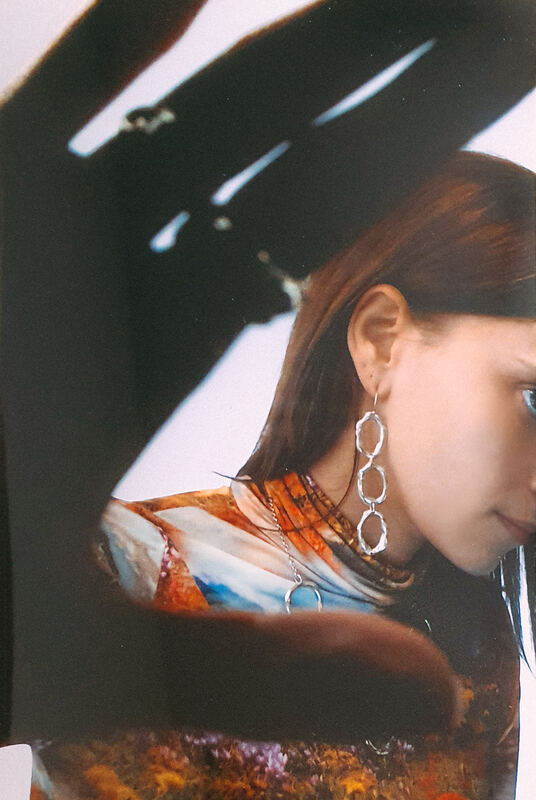 An arm raised and its shadow, a long cell earring catching the light