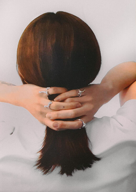 Seen from behind, hands holding her hair, rings on several fingers